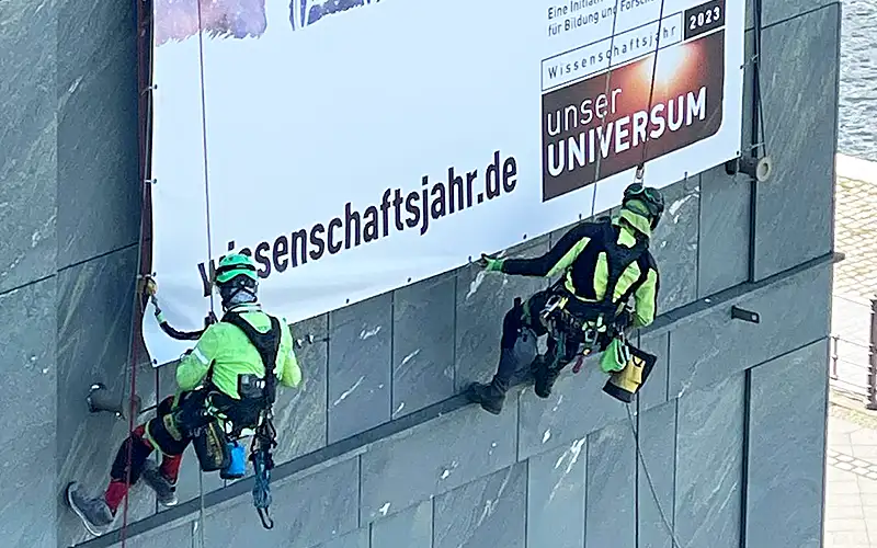 aufsteller reboard wabenplatte plattendruck produktion unternehmen referenz montage fassadenbanner mit kletterer gebaeudefassade bannerdruck